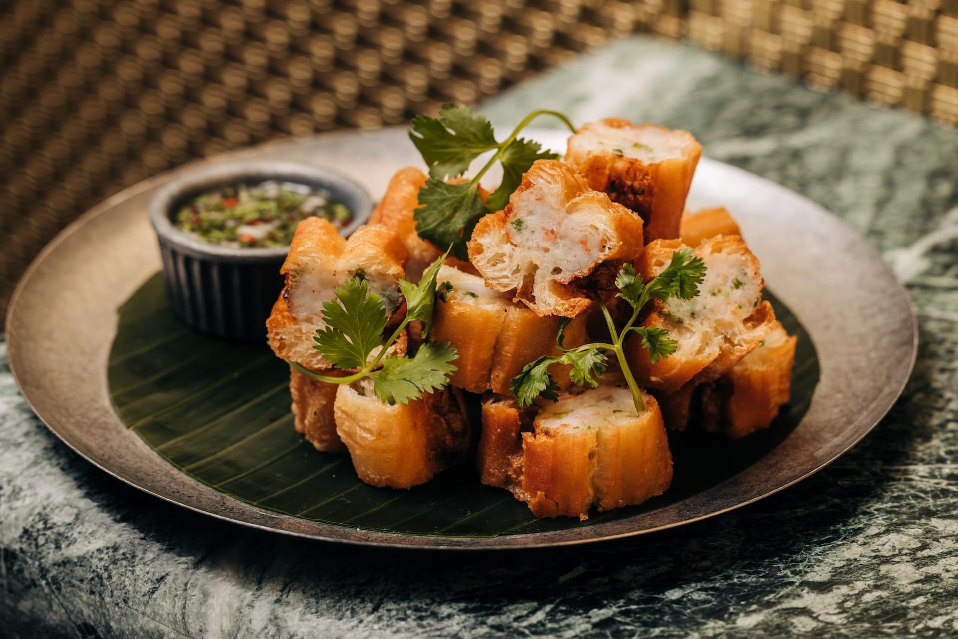 A plate of sliced prawn toast garnished with cilantro, accompanied by a small dipping sauce on the side.